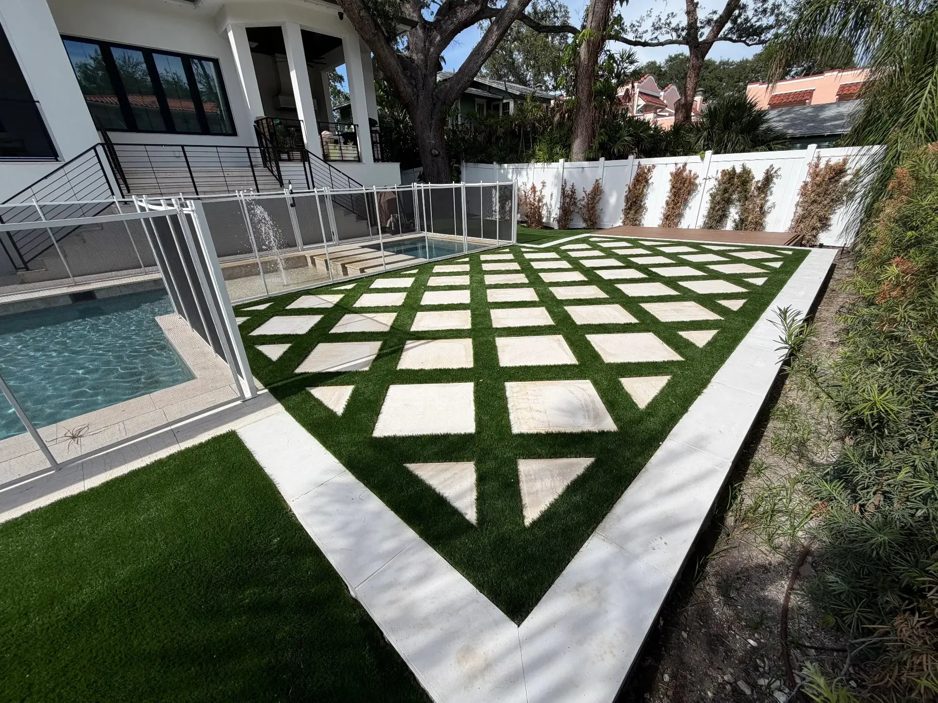Artificial turf laid in a diamond grid between white pavers beside a backyard pool