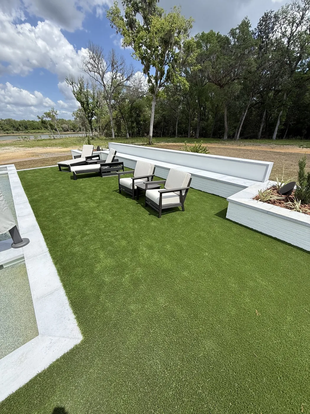Artificial lawn beside a pool with lounge chairs and a built-in bench